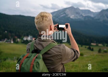 Jeune homme avec sac à dos prendre une photo sur le sommet des montagnes Banque D'Images