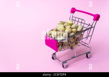 Petit chariot miniature en acier inoxydable avec pistaches à l'intérieur sur fond rose. Shopping, centre commercial, business concept Banque D'Images