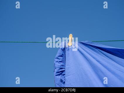 Un chiffon jaune fixe sur une ligne de lavage avec une feuille bleue et un fond bleu ciel. Banque D'Images