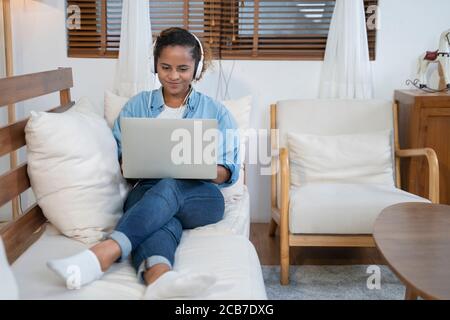 Femme souriante avec casque et ordinateur portable assis à la maison. Banque D'Images