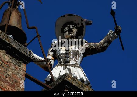 Dire l'heure à toute la ville. Une figure automatisée en bois, vêtue de costume de clown métallique, frappe les heures au sommet d'une tour, la Torre di Pulcinella (Tour de «Jr Punch»), sur la Piazza Michelozzo, Montepulciano, Toscane, Italie. Pulcinella était un personnage qui est apparu dans la commedia italienne dell’arte en 1600s. Banque D'Images