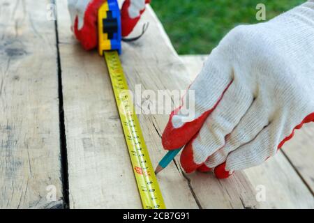 Un homme en gants de travail mesure la longueur de la planche et la marque avec un crayon. Banque D'Images