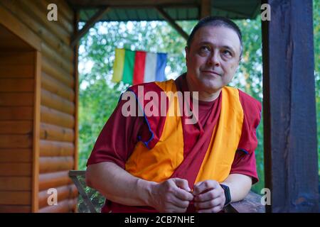 monk lama est debout sur le porche et tient un rosaire en bois dans sa main. Il porte un bracelet de fitness moderne Banque D'Images