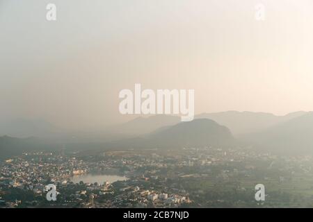Vue surélevée du lac Saint et de la ville environnante avec les collines d'Aravalli en arrière-plan sous le ciel brumeux à la pause du jour à Pushkar, Rajasthan, Inde. Banque D'Images