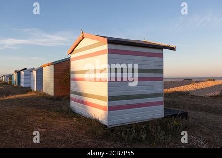 Le soleil couchant sur l'arrière de quelques cabanes de plage anglaises sur une plage dans le Kent. Banque D'Images