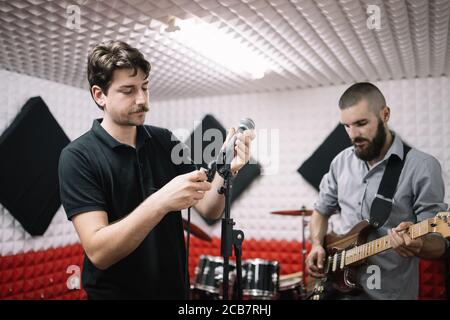 Jeune homme qui branche le microphone sur son support dans un studio de musique Banque D'Images