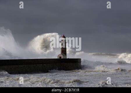 Grandes vagues blanches sur les jetées et le phare contre un ciel sombre et nuageux avant la pluie. Col du fleuve Douro, Porto, Portugal, pendant la tempête de la mer. Banque D'Images