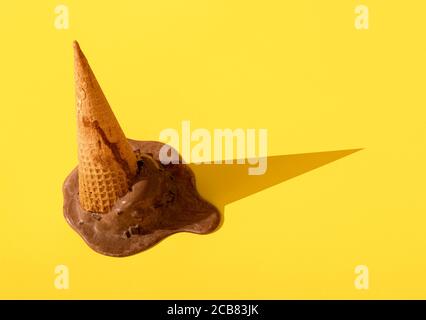 Glace au chocolat tombée dans un cornet de gaufres, fondant sur un fond jaune sans couture. Gros plan de la glace à l'envers. Dessert congelé d'été. Banque D'Images