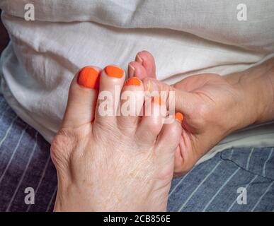 Une main tenant le pied d’une vieille femme, après avoir peint les cinq orteils dans une peinture orange vif pour les ongles. Banque D'Images