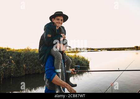 Le père et son fils s'amusent tout en pêchant. Garçon de l'adolescence heureux et sourire, asseyez-vous sur les épaules du père. Banque D'Images