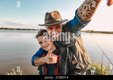 Le père prend le fils et prend le selfie, qui se tiendra sur la table à la maison comme photo pour la mémoire. Ils Amuse-toi bien. Arrière-plan lac. Banque D'Images