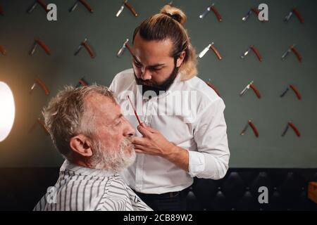 professionnel talentueux barbier va faire une nouvelle coiffure à un vieux client, travail, profession, profession. gros plan vue de côté photo Banque D'Images