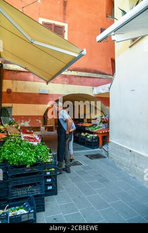 Extérieur d'une épicerie avec des fruits et des légumes exposés dans une ruelle étroite et le épicier avec un masque contre le coronavirus, Ligurie, Italie Banque D'Images