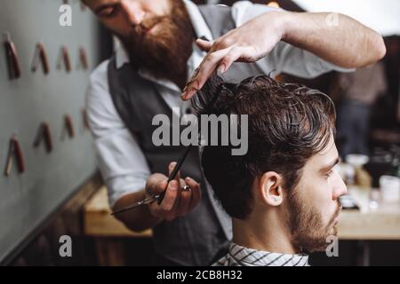 Barber à l'aide de ciseaux et de peigne. Homme avec barbe en coupe dans le salon de coiffure. Concept de salon de coiffure moderne. Banque D'Images
