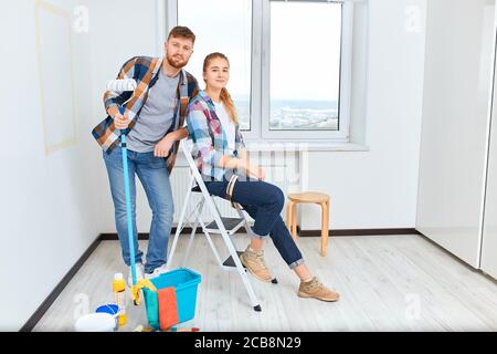 Portrait de couple souriant peint à la maison, tenant le rouleau de peinture et le pinceau, regardant l'appareil photo. Banque D'Images