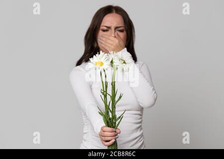 Studio portrait de la femme brune couvrant son nez, ayant une réaction allergique aux fleurs camomille, foyer sélectif. Allergie. Banque D'Images