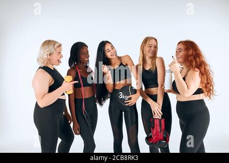 Les jeunes filles de fitness en vêtements de sport riant, se regardent l'une l'autre. Portrait og belles filles. Différentes nations, tailles, couleurs. Un mode de vie sain Banque D'Images