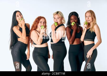 Jeunes filles séduisantes mangeant la pomme verte posant en studio, fond blanc. Promotion d'un mode de vie sain Banque D'Images