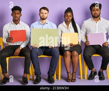 groupe diversifié de jeunes multiculturels assis sur des chaises avec des bulles de pensée dans les mains regardant dans la caméra en attente de travail entretien Banque D'Images