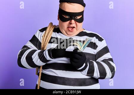 Joyeux gras excité jeune homme avec une corde sur son épaule tenant l'argent, le comptant. Portrait gros plan. Isolé fond bleu. studio tourné Banque D'Images