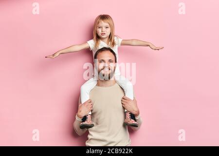 blonde belle fille avec bras étirés ayant un repos sur l'épaule de son père, fille jouant un avion avec un papa, intérêt, passe-temps Banque D'Images