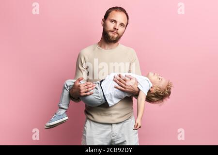 homme barbu essayant de calmer son enfant méchant. photo rapprochée. arrière-plan rose isolé, portrait rapproché. malheureux homme déprimé tenant une cryi malade Banque D'Images