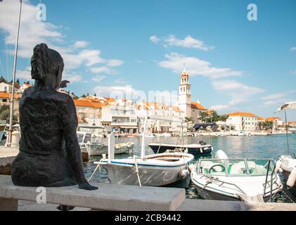 Statue d'une petite fille pointant vers le clocher de la petite ville côtière de Sutivan, sur l'île de Brac, Croatie. Prise de vue large avec le port et le Banque D'Images