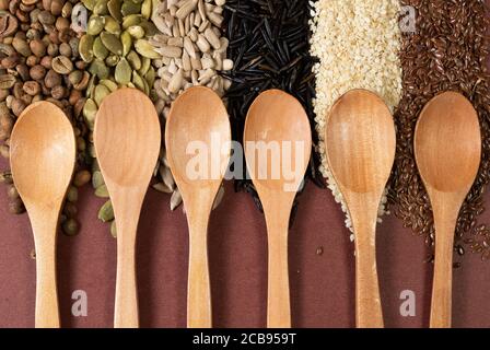 Six cuillères en bois sur une surface de différentes graines et arrière-plan marron Banque D'Images