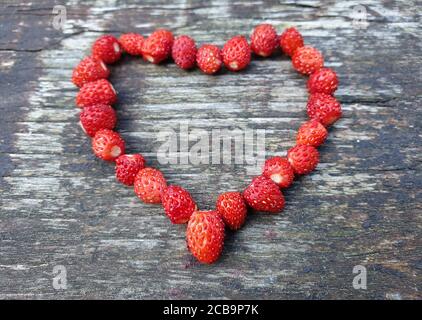 Fraises sauvages rouges fraîches en forme de coeur, sur bois vieilli. Concept de coeur symbolisant l'amour pour la nature et l'environnement. Fraîchement cueilli f Banque D'Images