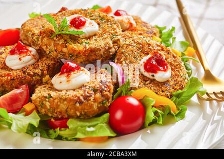 gros plan des hamburgers végétariens, des galettes de légumineuses, des oignons et des légumes verts avec une croûte de chapelure panko servie sur une assiette blanche avec une salade fraîche et une tombe Banque D'Images