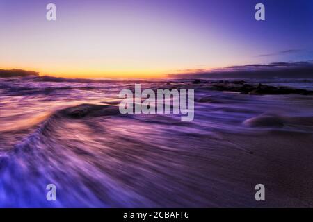 Queue de vague sortante sur les sables de la plage de Bronte à Sydney à l'aube face au soleil et à l'océan Pacifique. Banque D'Images