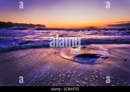 Plage de sable de Bronte sur la côte est de la banlieue de Sydney de l'océan Pacifique au lever du soleil avant l'aube avec vagues d'eau floues autour des rochers. Banque D'Images