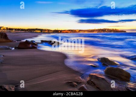 Sables et rochers de la plage de Bondi à Sydney au lever du soleil avec vagues floues et front de mer de maisons résidentielles sur la tête de Bondi Nord. Banque D'Images