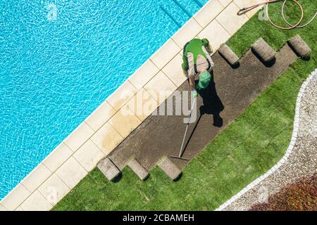 Paysagiste professionnel caucasien installant des tourfs d'herbe neuf de marque autour de la piscine résidentielle. Râtelage du sol avant l'installation. Jardinage et la Banque D'Images