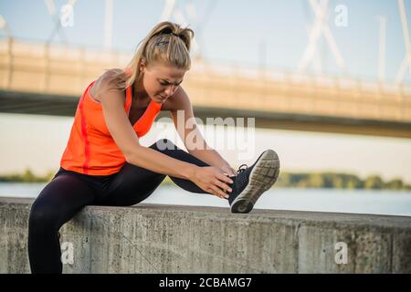 La jeune femme a de la douleur dans sa cheville tout en faisant de l'exercice et du jogging à l'extérieur. Banque D'Images