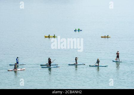 Lyme Regis, Dorset, Royaume-Uni. 12 août 2020. Météo Royaume-Uni. Paddle-boarders sur la mer calme à la station balnéaire de Lyme Regis à Dorset sur un autre jour chaud chaud chaud et ensoleillé que la vague de chaleur continue. Crédit photo : Graham Hunt/Alamy Live News Banque D'Images