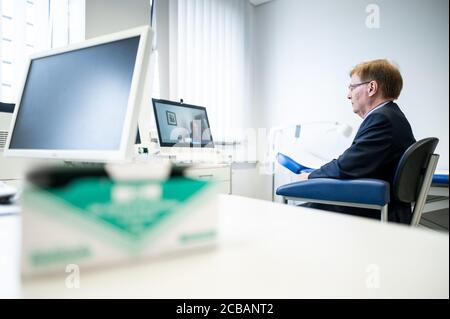 Attendorn, Allemagne. 12 août 2020. Peter Biesenbach (CDU), ministre de la Justice de la Rhénanie-du-Nord-Westphalie, est assis devant un écran lors d'une conférence vidéo sur la télémédecine. Biesenbach présente le projet pilote actuel de télémédecine dans les prisons. Grâce à la technologie numérique, les détenus peuvent accéder à des soins médicaux en dehors des heures de bureau et à l'intérieur des murs de la prison 24 heures sur 24, grâce à des transmissions en direct. Sept des 36 prisons de NRW participent au projet pilote. Credit: Fabian Strauch/dpa/Alay Live News Banque D'Images