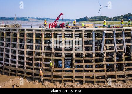 Des travailleurs du Canal and River Trust descendant à marée basse pour effectuer des réparations à la jetée en bois à l'entrée de Sharpness New Dock sur la rivière Severn à Gloucestershire. L'association caritative Waterways Canal and River Trust utilise une grue d'araignée pour amener des planches de chêne greenheart qui seront fixées en place par une équipe descendue sur des cordes suspendues au-dessus du lit de rivière boueux à marée basse. Banque D'Images