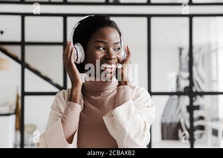 Image de l'incroyable gai heureux jeune femme africaine écoutant de la musique avec un casque à l'intérieur de la maison Banque D'Images