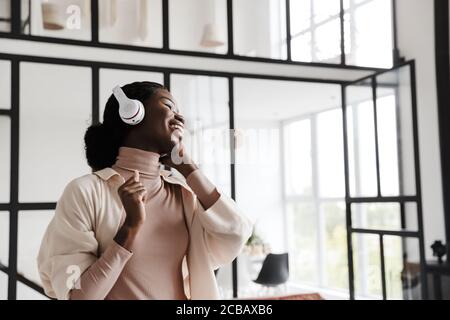 Image de l'incroyable gai heureux jeune femme africaine écoutant de la musique avec un casque à l'intérieur de la maison Banque D'Images