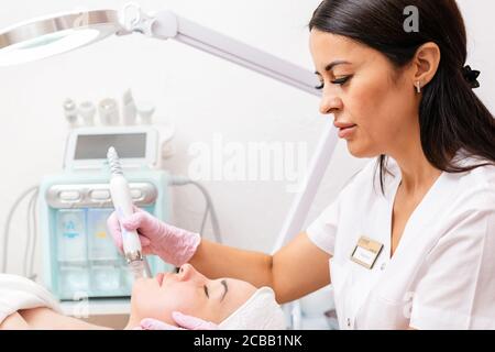 Salon de beauté. Le cosmétologue fait un gommage de l'eau pour le client. Dispositif pour la procédure en arrière-plan.soins de la peau et beauté professionnels Banque D'Images