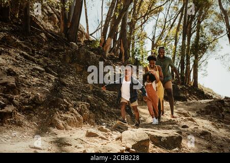 Une jeune famille s'élançant sur un sentier de montagne rocheux. Deux enfants en train de courir avec leurs parents sur un sentier en forêt. Banque D'Images