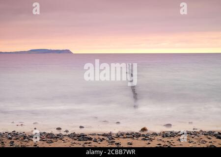 Coucher de soleil sur une eau douce avec vue sur le brise-lames et ciel nuageux. Photographie à temps d'obturation long avec de l'eau brumeuse et une atmosphère mystique Banque D'Images
