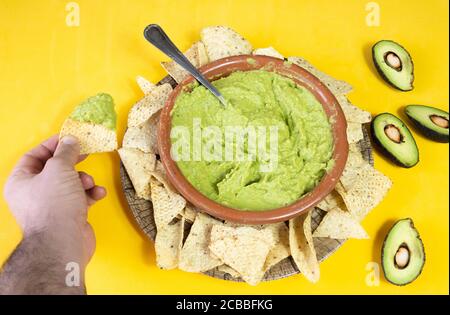 Homme mangeant un délicieux nachos mexicain avec guacamole sur un arrière-plan jaune Banque D'Images