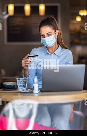 Portrait de jeune femme d'affaires portant un masque tout en faisant des achats en ligne et le paiement par cartes de crédit. Nouveau mode de vie normal pendant la pandémie de Covid-19. Banque D'Images