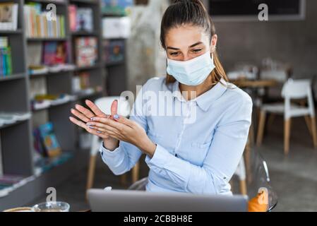 Portrait d'une jeune femme avec masque chirurgical en utilisant du gel désinfectant pour les mains au restaurant. Antiseptique, virus pandémique Corona, concept d'hygiène et de soins de santé. Banque D'Images