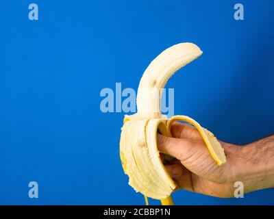 Gros plan d'une main mâle tenant une banane pelée arrière-plan bleu Banque D'Images