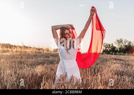 Photo à l'extérieur d'une jeune fille au gingembre en robe blanche tenant un foulard rouge en vol. Banque D'Images