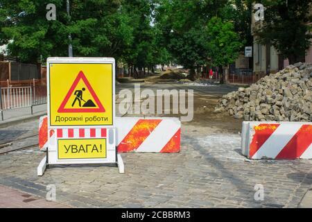 Route du centre-ville fermée par des barrages routiers en pierre pendant la reconstruction. Le panneau jaune avec les mots en ukrainien signifie TRAVAIL DE ROUTE, ATTENTION. Rue de la ville Banque D'Images