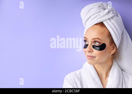 Charmante fille en peignoir et serviette posant avec des taches noires, l'industrie de la beauté, les soins de la peau. Isolé sur fond violet Banque D'Images